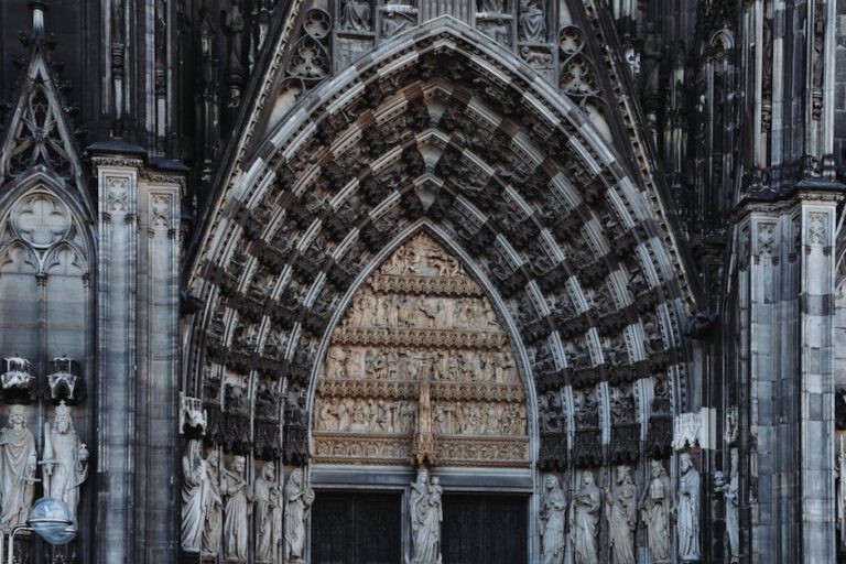 Cologne MICE events - Detailed view of the intricate Gothic entrance of Cologne Cathedral, showcasing religious statues. - Photo by Masood Aslami
